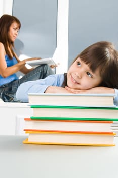 Photo of schoolkid on heap of colorful books with her mother at background