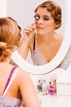 Image of pretty female looking in mirror while curling her eyelashes