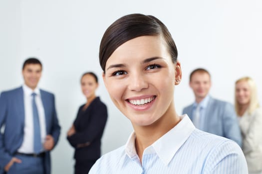 Young businesswoman looking at camera and smiling against her colleagues