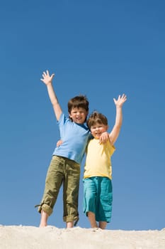Photo of happy boys waving on sandy beach and looking at camera