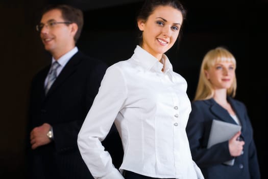 Portrait of three business people on the black background with a beautiful smiling businesswoman at the front
