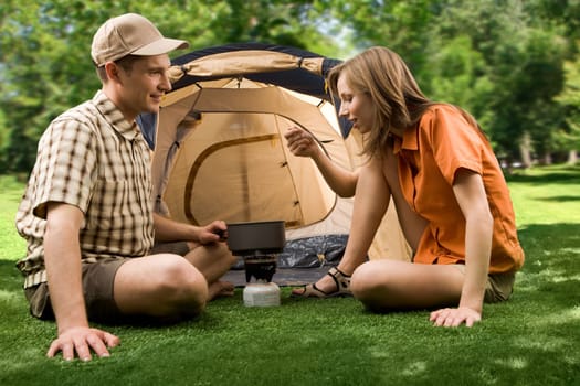 Photo of cheerful girl holding cup while her boyfriend pouring tea into it in the park