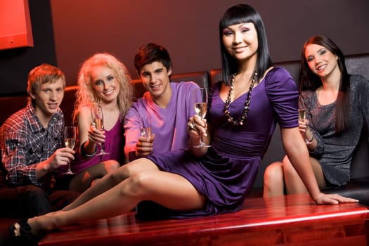 Image of glamorous woman with champagne sitting on table on background of her friends