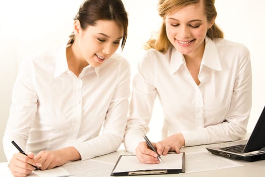 Photo of two business women working with documents and writing something on paper