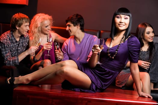 Elegant woman with champagne sitting on table on background of chatting people
