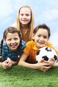 Image of happy friends lying on the grass with ball and looking at camera