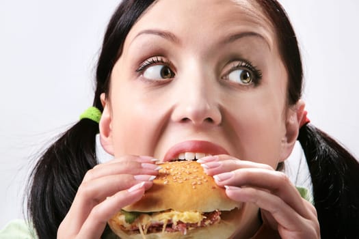 Image of hungry girl eating hamburger and looking aside