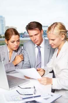 Image of successful businesspeople looking at document while discussing it in office