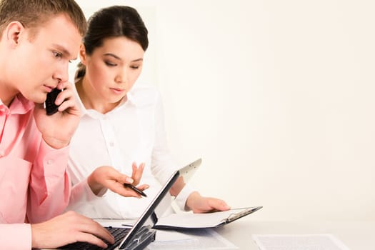 Photo of serious man making telephone call while his partner showing him something on laptop monitor during meeting