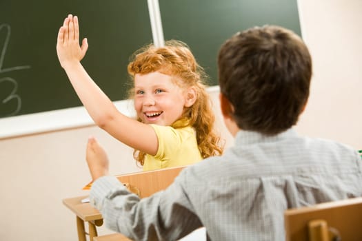 Photo of happy schoolgirl sitting and raising her hand at the lesson