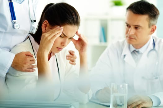 Portrait of woman with headache touching her temples with medical staff near by