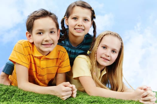 Image of happy friends lying on the grass and looking at camera