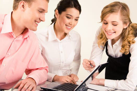 Photo of smart professional pointing at laptop screen while two colleagues looking at it with smiles