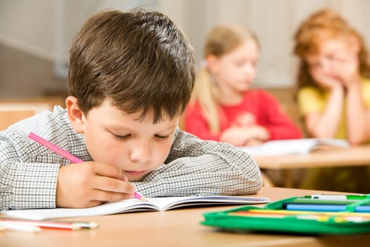 Portrait of bored pupil putting his head on desk and drawing something in copybook at lesson