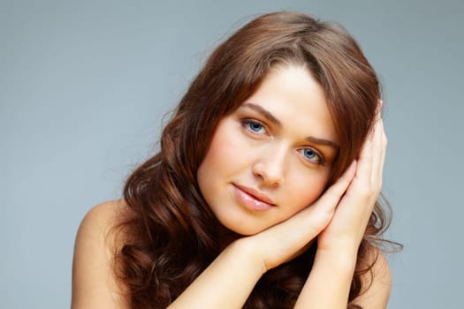 Fresh girl with hands by her cheek looking at camera over grey background