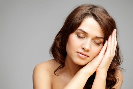 Fresh girl with closed eyes touching her cheek over grey background