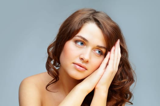 Fresh girl with hands by her cheek looking aside over grey background