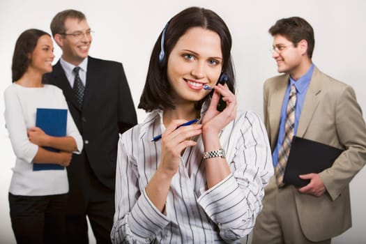 Portrait of  better telephone operator holding headset and pen on the background of  three businesspeople
