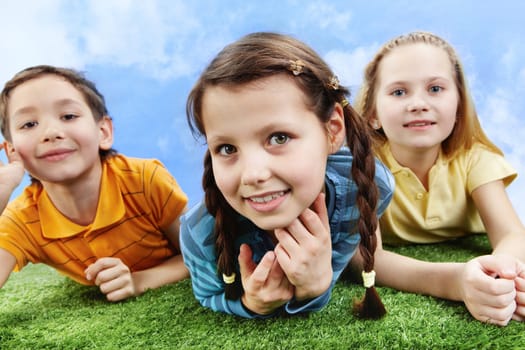 Image of happy girl lying on the grass and looking at camera with friends at background