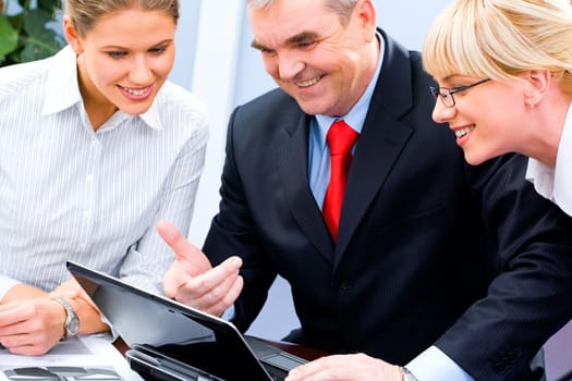 Photo of businessteam doing some computer work and looking at the laptop screen during meeting in the office
