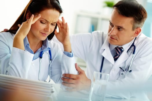 Portrait of woman with headache touching her temples with colleague near by