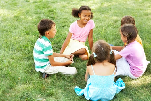Portrait of cute kids seated on green grass and chatting
