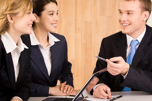 Portrait of happy businessman speaking to his colleagues at meeting while they listening to him with smiles