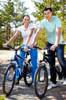 A young couple on bicycles looking at camera and smiling