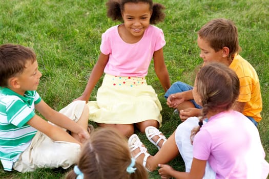 Portrait of cute kids seated on green grass and chatting