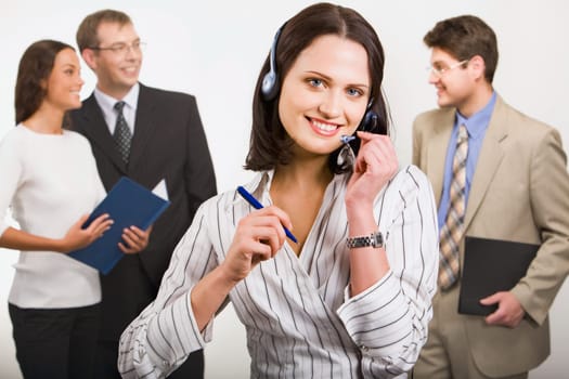 Beautiful telephone operator is holding headset and pen on the background of  her working team