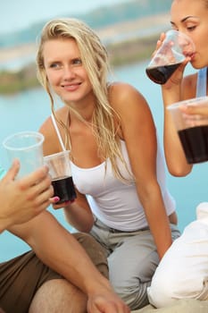Image of happy girl with drink surrounded by friends at beach party