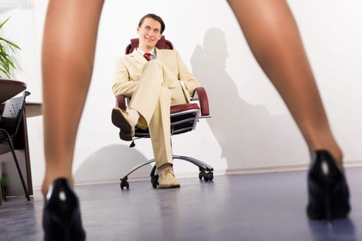 Image of slim female legs before businessman sitting in arm-chair and looking at them
