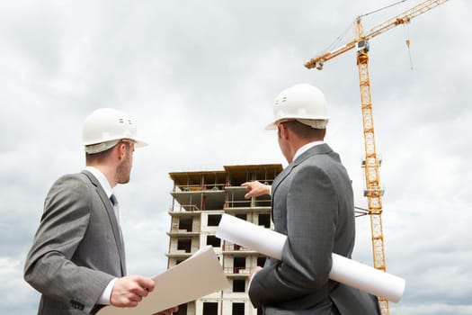 Photo of young engineer showing something to his partner at building site