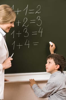 Portrait of diligent pupil looking at his teacher near blackboard while doing sums