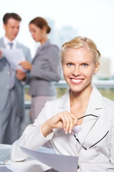 Confident businesswoman looking at camera at background of communicating people