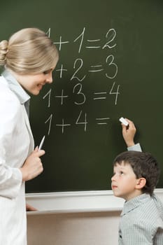 Portrait of diligent pupil looking at his teacher near blackboard while doing sums