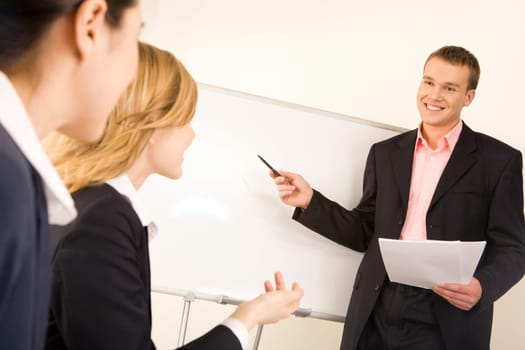 Photo of successful businessman standing at white board while two ladies looking at him during seminar