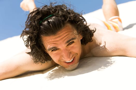 Happy guy lying on sand with outstretched arms and looking at camera on beach