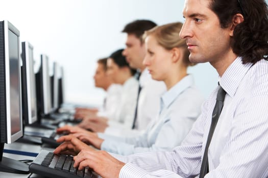 Photo of serious businesspeople typing and looking at monitors in line