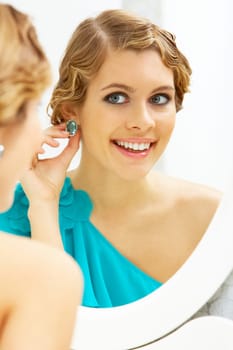 Image of pretty female looking in mirror and putting on earrings