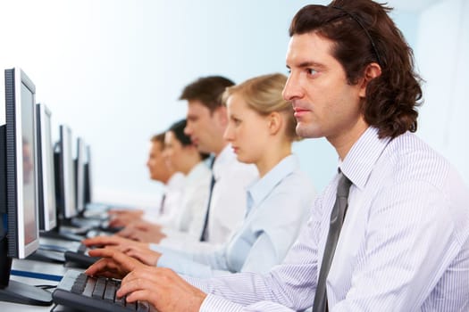 Photo of serious businesspeople typing and looking at monitors in line