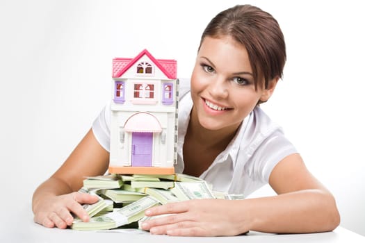 Portrait of lucky woman raking up heap of money with toy house on its top
