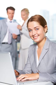 Confident businesswoman looking at camera while typing at background of communicating people