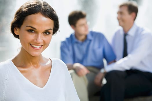 Successful young woman on the background of two businesspeople outside