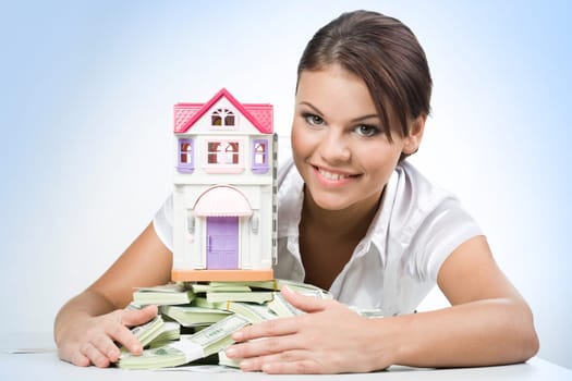 Portrait of beautiful woman touching heap of money with toy house on its top