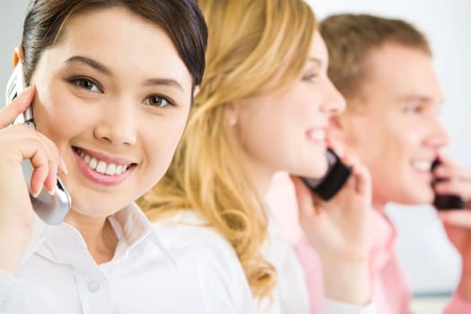 Face of smiling businesswoman making phone call and looking at camera with smile on background of two phoning people