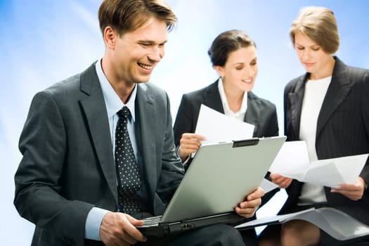 Confident smiling businessman sees the decision of a question   in the laptop on the background his coworkers