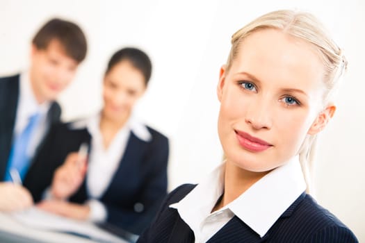 Portrait of blonde businesswoman looking at camera on background of working people