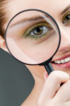 Close-up of young woman looking at camera through magnifying glass