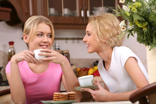 Two smiling girls have tea with tasty cookies in the kitchen